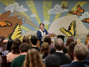 An author reads at a podium in a packed venue.