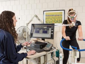 One student is on a stationary bike while the other student is monitoring breathing and heart rate at a computer monitor.