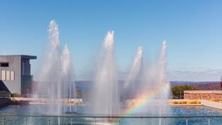 A rainbow appears among six fountains. 