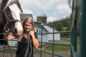 Close photo of Kendra Hubal standing next to horse, barn in background