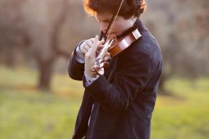 A person playing a violin outside, with grass and trees in the background