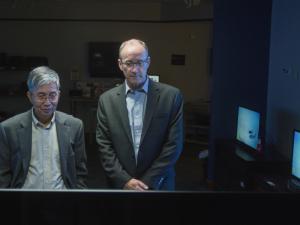 Chin Wan Tang and Steven Van Slyke stand in a darkened room surrounded by OLED monitors.