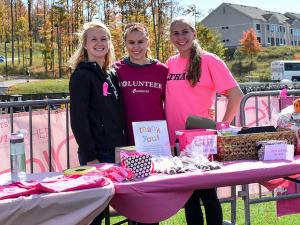 Three young women stand together and smile while standing outdoors at a table covered in raffle prizes.