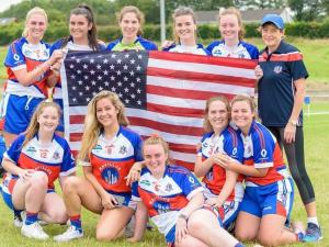 A group of women in athletic uniforms pose with the U.S. flag