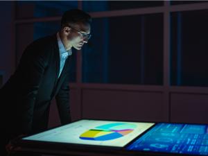 A man in a suit looks at graphs on a screen