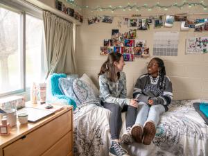two girls sitting on a bed in a dorm room