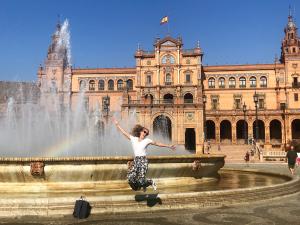 A person jumps in the air in front of a fountain and plaza in Seville, Spain