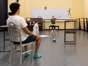 A student sits in a chair looking at another student in a chair directing them.