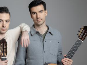 Two people stand holding guitars