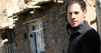 A man wearing headphones standing in front of stone buildings