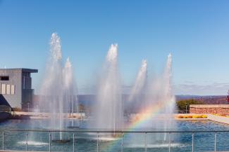 A rainbow appears among six fountains. 