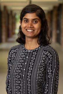 Prof. Mondal is wearing a black aand white shirt and standing against the backdrop of an empty hallway.