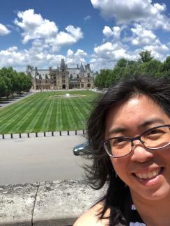 Melody with sunny blue skies and white puffy clouds standing at the end of the outdoor main lawn overlooking the facade of Vanderbilt's Biltmore estate and mansion in the background. Location: Asheville, NC