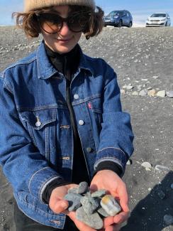 Alexis in denim jacket, sunglasses, and hat, holding rocks 