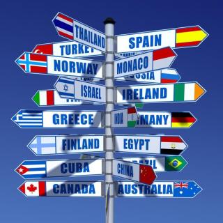 Signpost with signs to multiple countries pointing in many different directions, against a blue sky.