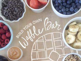 Build your own waffle bar sign surrounded by bowls of fruit and other toppings.