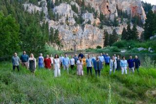 a group of people stand in a meadow in front of a rocky cliff face