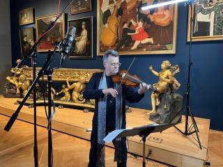 A man plays a violin surrounded by museum artwork