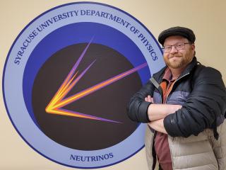 Photograph of Dr. Denver Whittington with the logo of the Syracuse University neutrino group.