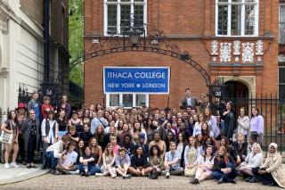 A group of Ithaca College students outside of the Ithaca College London Center, a red brick building with white trim. Students are posed in front of a wrought iron gate and archway that marks the entrance to the London Center building.