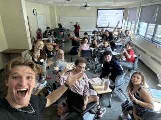 A selfie of a classroom of people waving at the camera. The people pictures are Resident Assistants.