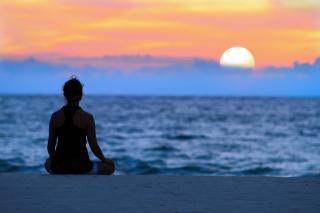A picture of someone meditating on the beach during sunrise.
