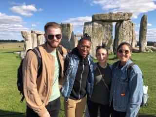 Four college students posing in front of Stonehenge in the UK