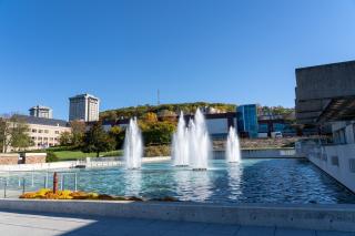 A picture of the Ithaca College fountains in the sunshine with South Hill, academic buildings and the Towers in the background.