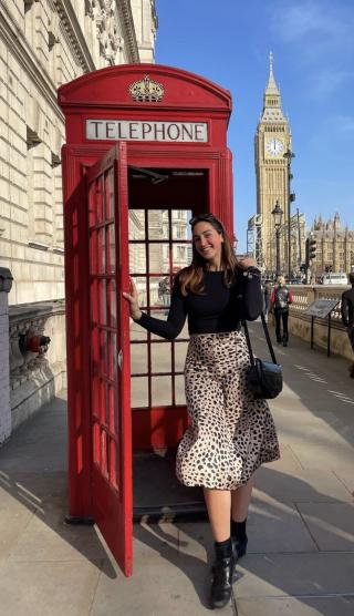 An Ithaca College student standing in front of an iconic red British phone booth in London, with Big Ben in the background