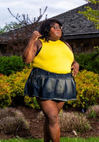 Ashanti is posing for photo outside of Muller Chapel. Ashanti is wearing a skirt and yellow sleeveless top. Ashanti is looking off to the right of the image.