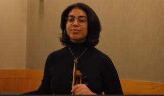 Laura is posing for camera with viola in hand. Is wearing black turtleneck sweater and glasses. Has shoulder length dark hair and is looking at camera, but not smiling.
