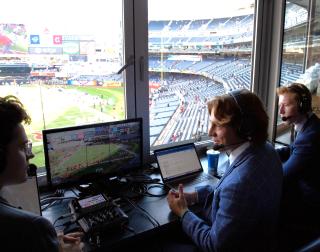 Three people in a broadcast booth at a stadium.