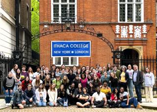 A group of college students posing in front of a brick Victorian townhouse in London.