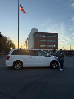 Photo of white mini-van to take voters to the polls in front of sunset and American flag.